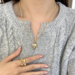 Close-up of golden heart pendant necklace and geometric ring on grey sweater