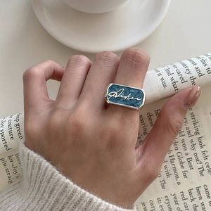 Close-up of a silver rectangular ring featuring blue celestial enamel and script detail