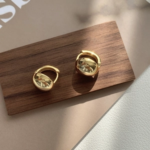 Close-up of polished gold chunky hoop earrings on a textured wooden and leather surface