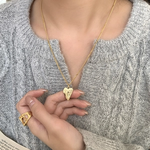 Irregular heart pendant necklace in gold finish with hammered texture on grey sweater