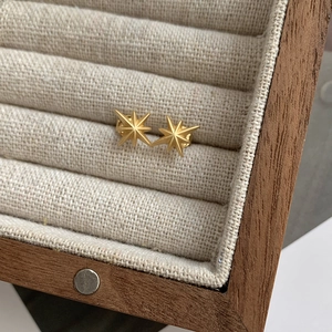 Macro shot of gold octagram star stud earrings displayed in a luxury wooden jewelry box