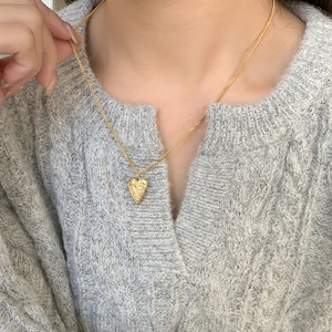 Detail of gold irregular heart pendant necklace with hammered texture on a gray sweater