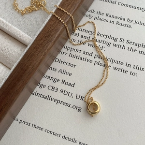 Detailed view of a minimalist gold ring pendant on a delicate link chain over jewelry box