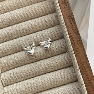 Macro detail of silver bow and heart earrings on a beige linen jewelry display tray