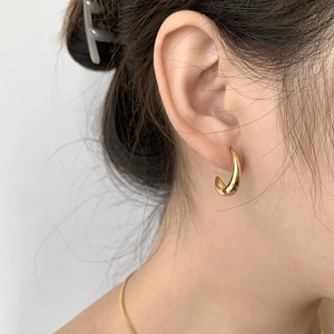 Primer plano de un pendiente en C dorado pulido en una modelo con estilo minimalista