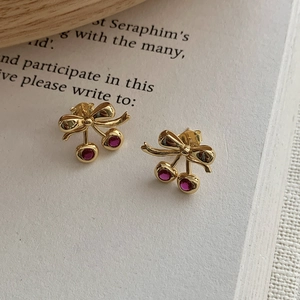 Vue détaillée des boucles d'oreilles cerises en argent S925 avec pierres rouges sur un livre