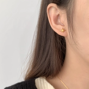 Close-up of minimalist gold starburst stud earrings with a matte finish on a model