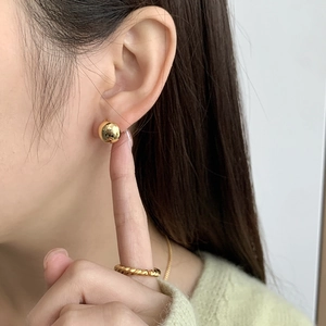 Close-up of polished gold ball earrings and twisted rope ring worn by a model