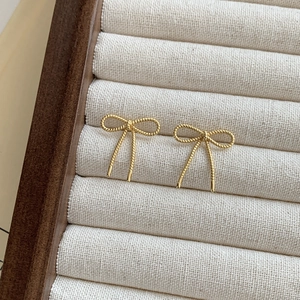 Vue détaillée de boucles d'oreilles nœud dorées avec texture torsadée sur présentoir beige