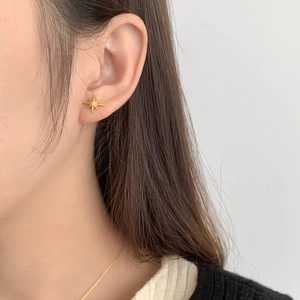 Detail of minimalist gold starburst stud earrings with a refined matte metal finish