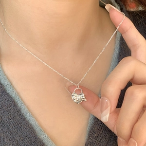 Gros plan du collier avec pendentif cœur et nœud en argent 925 porté sur un tricot gris