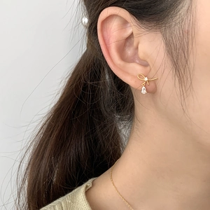 Close-up of a gold knot drop earring with a teardrop zircon worn by a model