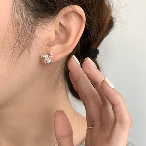 Close-up of S925 sterling silver bow and heart earrings worn by a model