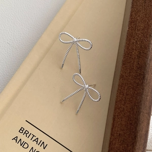 Gros plan de boucles d'oreilles nœud en argent avec texture torsadée sur carte beige