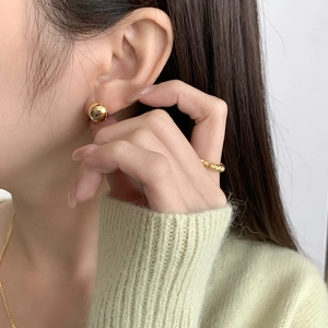 Close-up of polished gold ball stud earring and twisted ring on model with green knitwear