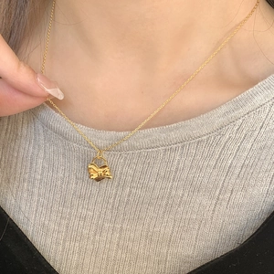 Gros plan d'un élégant collier à pendentif nœud doré porté avec un pull en maille gris
