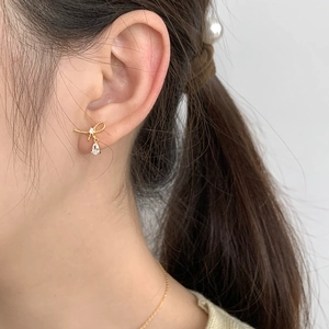 Close-up of elegant gold bow earrings with a teardrop crystal on female model