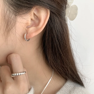 Gros plan de boucles d'oreilles géométriques et bague torsadée en argent sur modèle