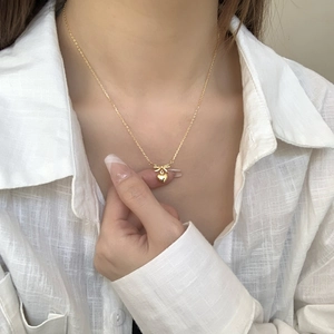 Close-up of a gold bow and heart pendant necklace worn on a woman's collarbone