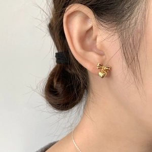 Close-up of golden bow and heart drop earrings worn by a model in a minimal style
