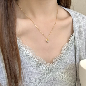 Close-up of a golden bow pendant with a white pearl on a delicate silver chain