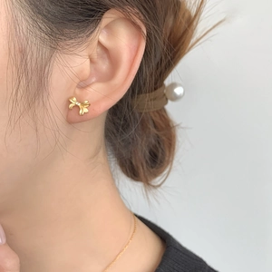 Élégantes boucles d'oreilles nœud en or mat avec petit diamant portées par un mannequin