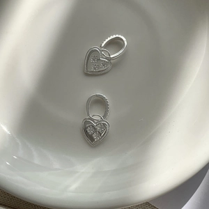 Macro detail of S925 silver heart earrings with star motifs on a ceramic dish