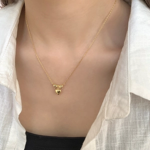 Close-up of gold bow and heart pendant necklace worn on a soft linen shirt