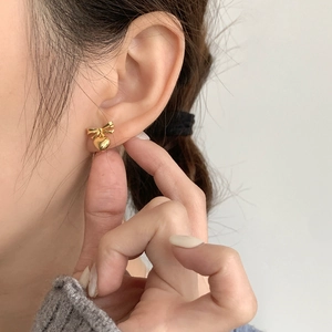 Close-up of elegant gold bow and heart stud earrings worn by a model in soft lighting