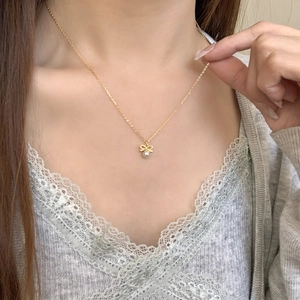 Close-up of elegant gold bow pendant necklace with a white pearl on a female neck