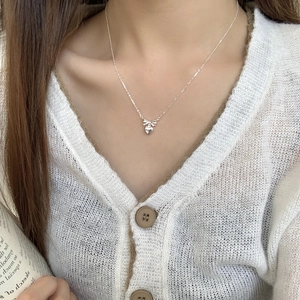 Detail shot of a delicate S925 sterling silver bow and heart pendant necklace on a model