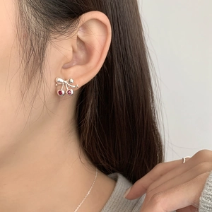 Détail des boucles d'oreilles cerise en argent S925 avec nœud papillon sur l'oreille