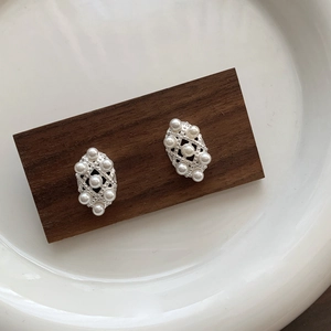 Detail of silver rhombus lace stud earrings with small pearls on a wooden block