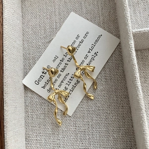 Macro view of gold heart stud earrings with ribbon bow pendants on a display card