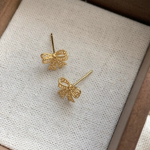 Elegant gold S925 sterling silver hollow lace bow stud earrings on a vintage linen background