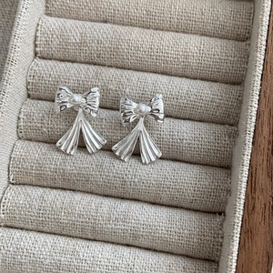 Gros plan détaillé d'une boucle d'oreille nœud argentée avec perle sur fond en lin beige