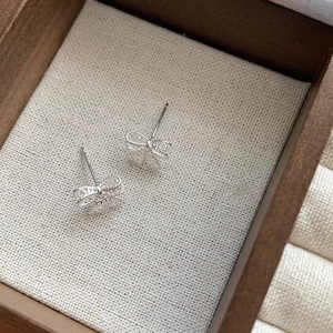 Macro view of delicate S925 silver hollow lace bow stud earrings on a beige fabric pad