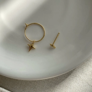 Detail of asymmetric gold star hoop earrings on white ceramic and linen background