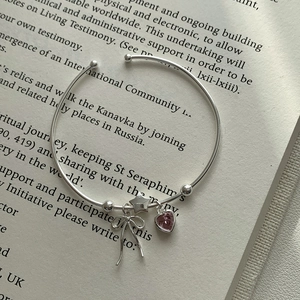 Detail of S925 silver cuff bracelet featuring pink heart zircon and bow charms on a book
