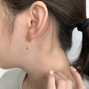 Close-up of golden asymmetric hoop earring with a delicate four-pointed star pendant
