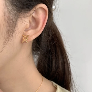 Close-up of golden X-shaped crossover stud earrings worn on an ear showing fine details