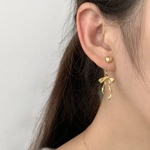 Detailed close-up of a model wearing a gold heart ribbon bow earring in a French vintage style