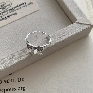 Close-up of polished silver bow ring with adjustable band on a minimalist vintage background