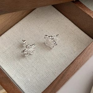 Detailed macro shot of 925 sterling silver hollow flower studs in a rustic wooden jewelry box