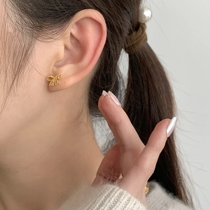 Detailed close-up of a golden lace bow stud earring worn on the earlobe