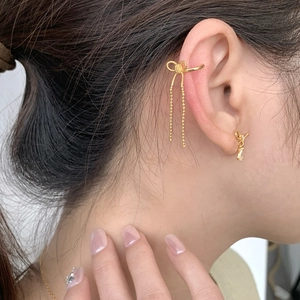 Detail of gold bow ear cuff with long tassels and zircon stud worn on ear