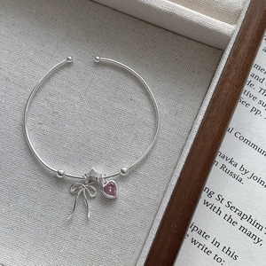 Detail of S925 silver bangle with pink heart gem, star, and bow charms on soft fabric