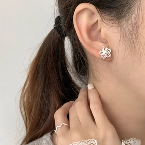 Macro detail of hollow floral 925 silver stud earrings and matching wavy ring on a model