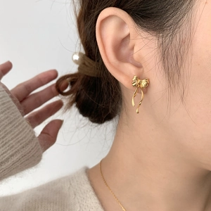 Boucles d'oreilles nœud dorées avec texture satinée portées par un mannequin femme