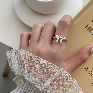 Close-up of a silver bow ring on a hand with lace sleeve and a cozy cafe backdrop